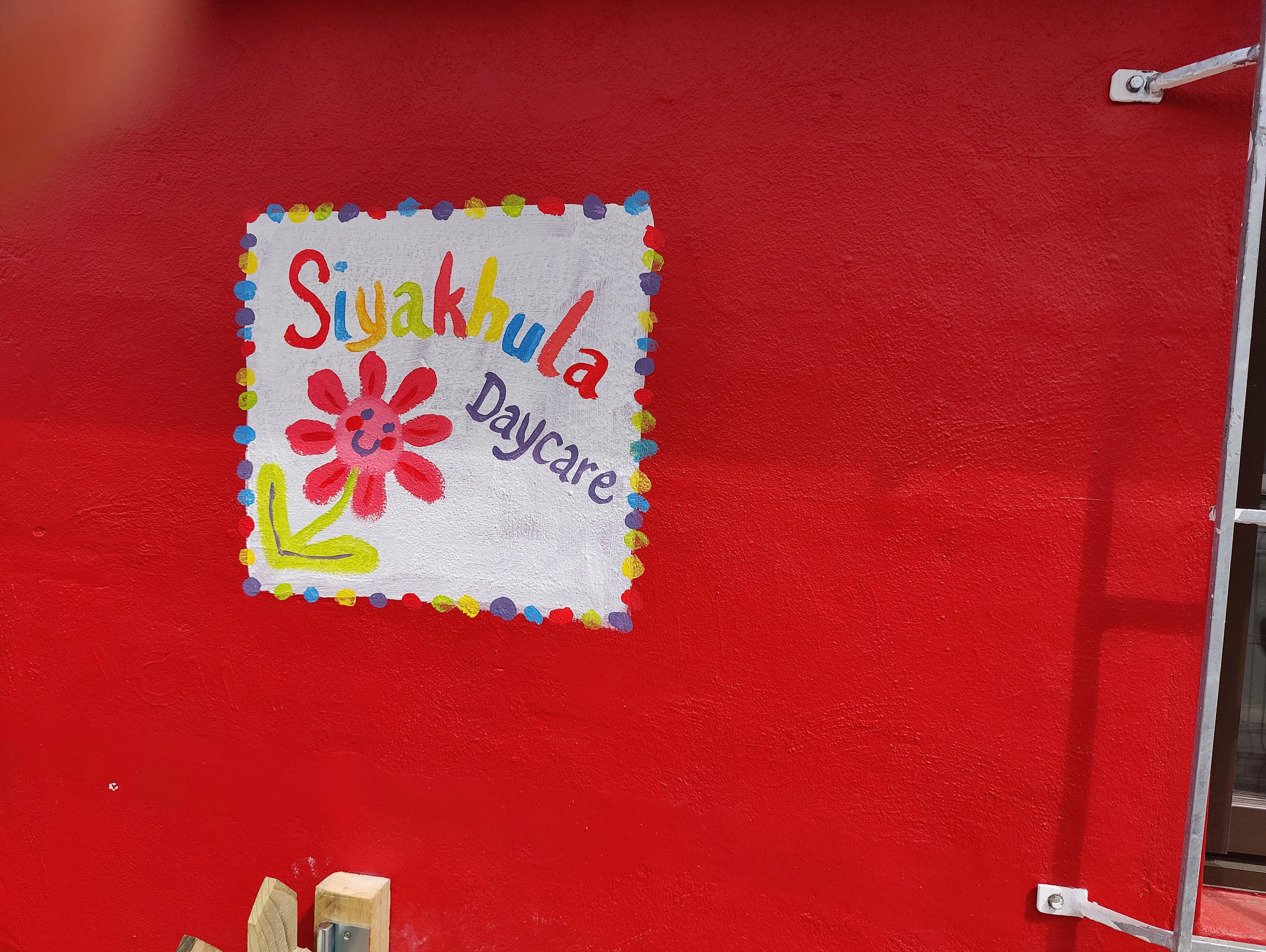 Handgemaltes Siyakhula Daycare Schild an der roten Wand